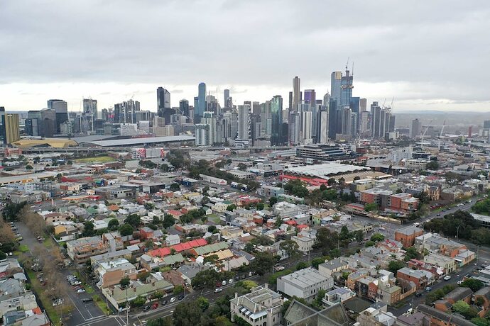 Older, low rise heritage buildings in the foreground and Melbourne's city towers in the background with a grey, cloudy sky.